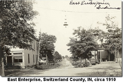 Black and white photograph showing a dirt road running off into the distance and an intersection in the foreground with a house on the left and a Post Office on the right; caption reads: 'East Enterprise, Switzerland County, IN, circa 1910'